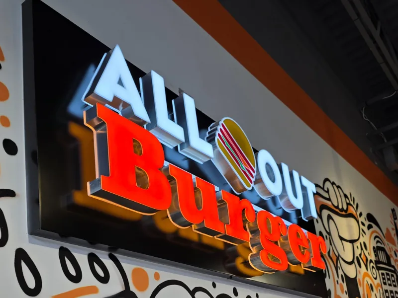 Illuminated All-Out Burger sign above a restaurant mural